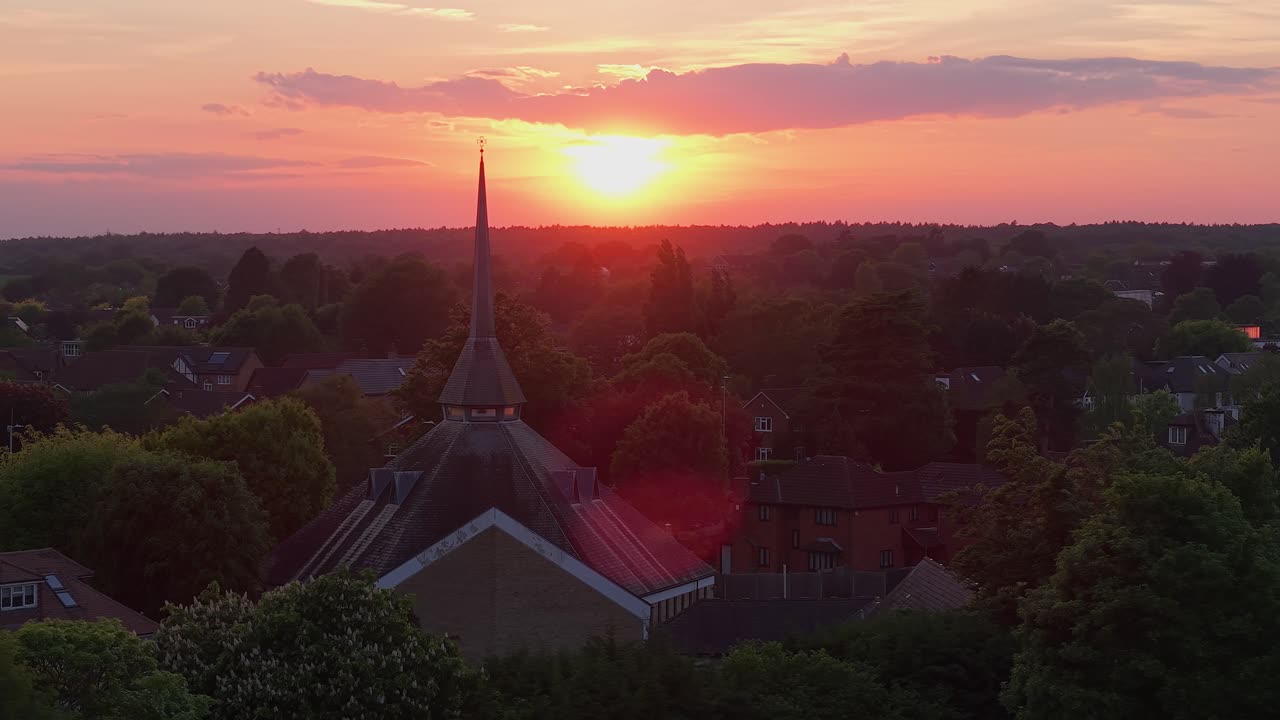 Aerial drone orbit at sunset captures St Bartholomew Church in St Albans under a vivid orange sky, blending historic architecture with warm evening light and serene atmosphere
