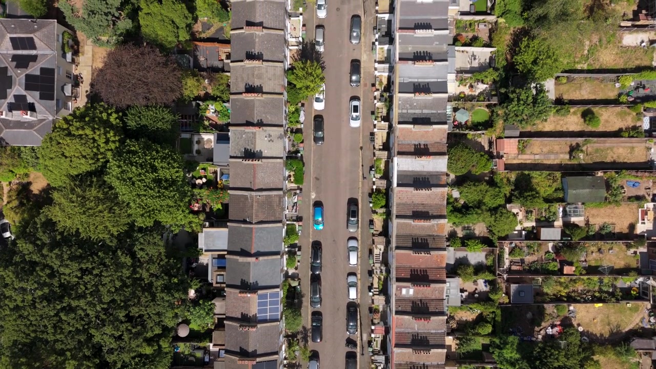 Vista aerea con drone di tetti di case a schiera e auto parcheggiate lungo una strada residenziale britannica