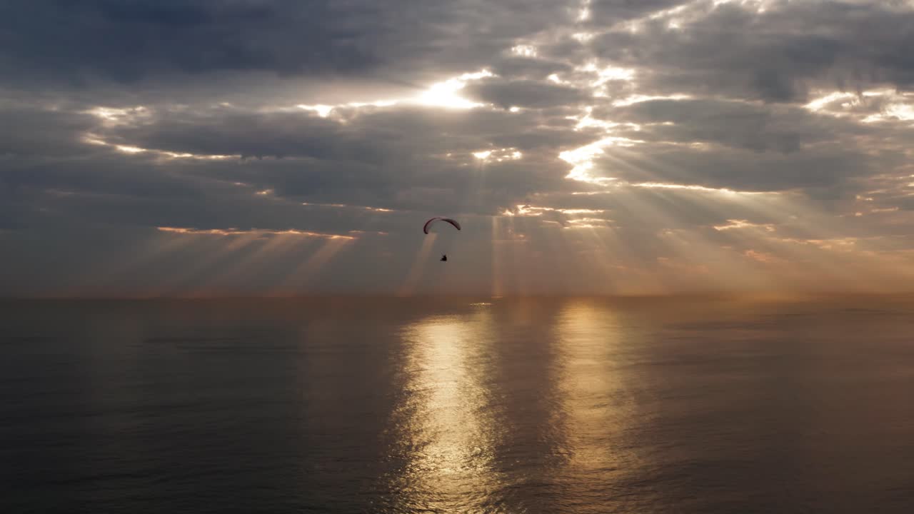 Paragliding into sunset seascape, with sun rays over ocean seascape. Freedom and adventure concept.