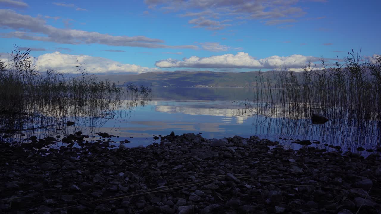 푸른 하늘에 흰 구름을 반사하는 물이 있는 잔잔한 호수의 바위 해안에 황혼