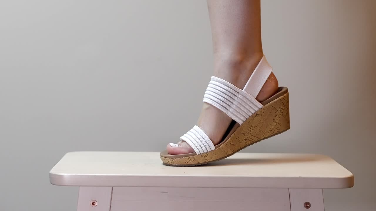 Mulher flexiona a perna com o pé usando saltos plataforma de cortiça brancos, movendo-se de um lado para o outro.