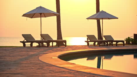 two sun umbrella and four deckchairs poolside with sea in background at sunset