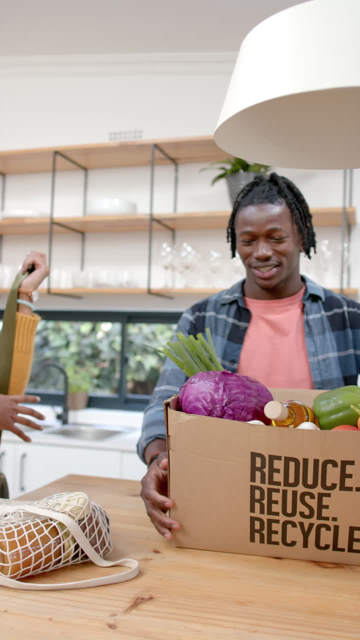 Vertical video of happy african american couple unpacking groceries in kitchen, slow motion