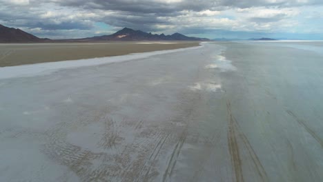 aerial view of big salt flats with the sky mirroring in them and mountains and clouds in the background