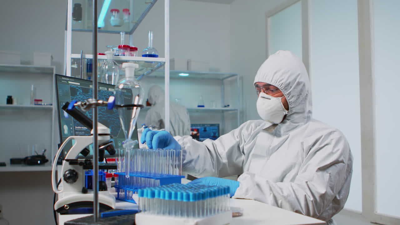 Biolog i PPE-dragt undersøger væskeprøve og taster på computer