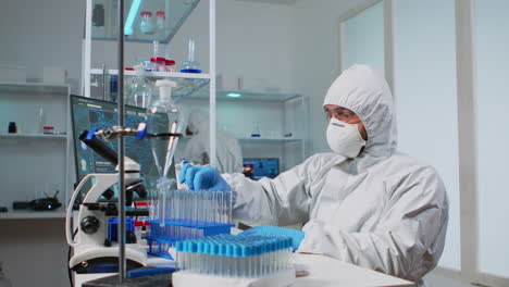 médico biólogo en traje de ppe comprobando muestra de líquido escribiendo en pc