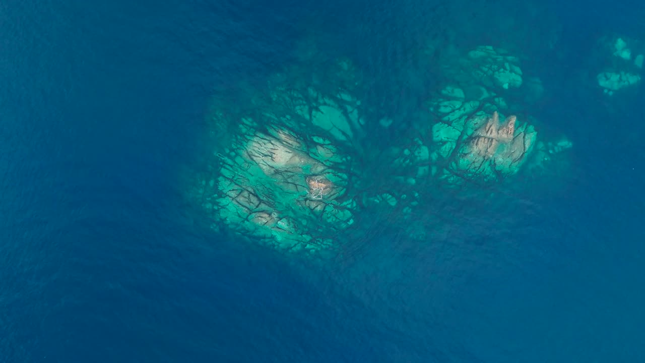 Aerial top-down view of shallow rocky seabed and reef structures under turquoise Mediterranean water near Porticello, Sicily, perfect for marine and coastal themes