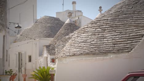 Charmante-Gasse-In-Alberobello-Mit-Weißen-Häusern-Und-Grünen-Pflanzen-Und-Einem-Roten-Auto