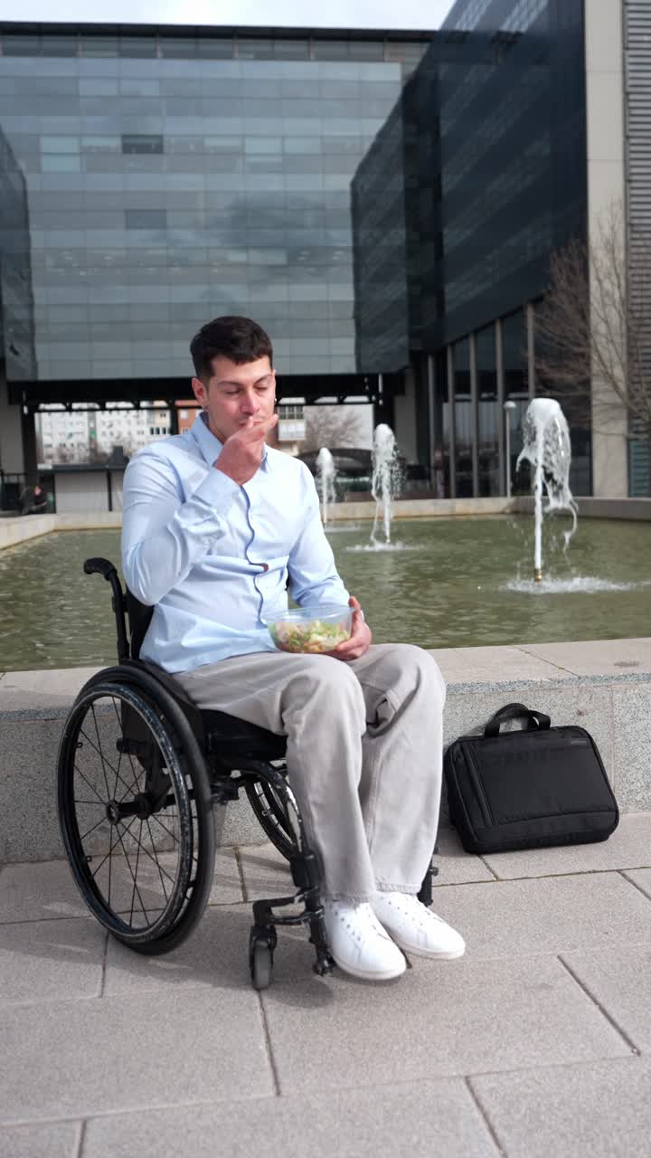 Young Man in Wheelchair Eating Salad Outdoors by Office Building