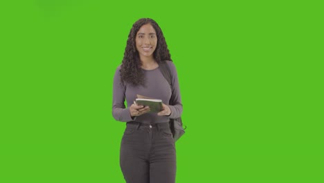 portrait of female college or university student writing in notebook against green screen smiling at camera