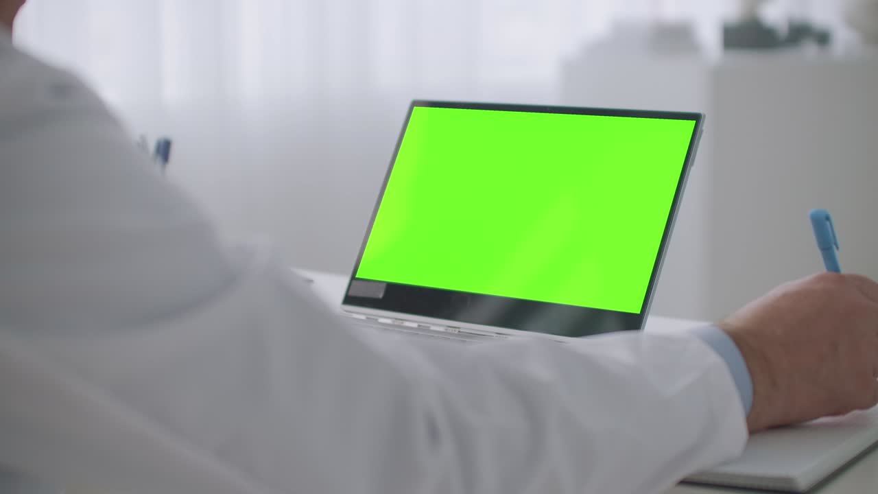 telemedicine service, consulting with best medical specialist online, laptop with green screen for chroma key technology on table, physician is writing notes