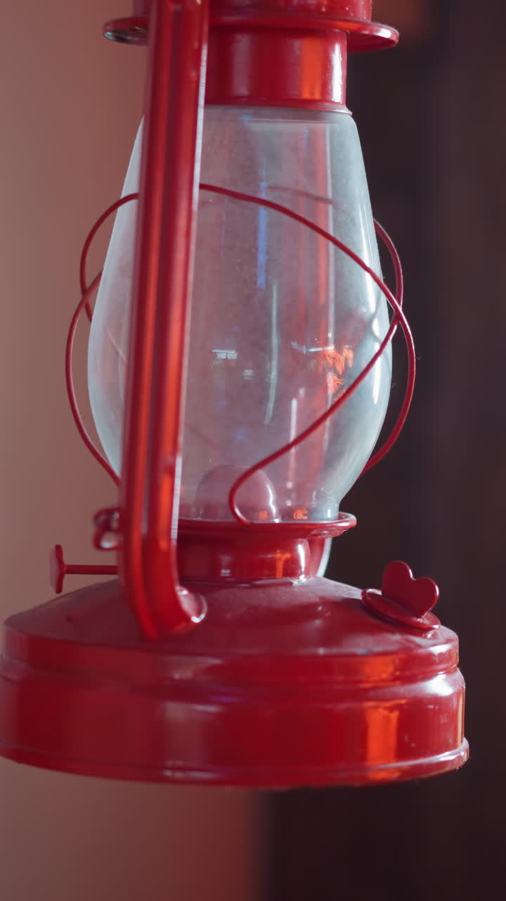 Close-up view of a vintage red lantern hanging on a wooden beam with a rustic background, the lantern's glass and metal structure are highlighted