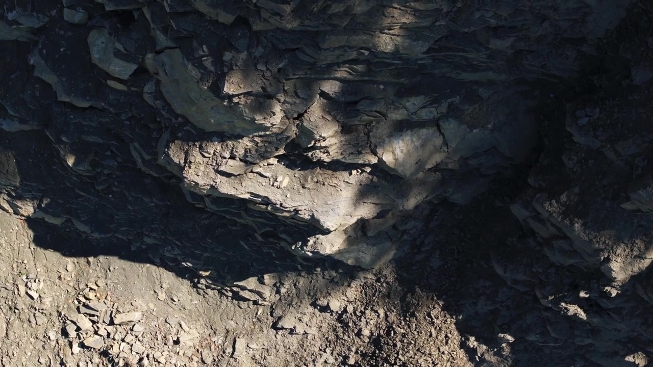 Blottede klippelag og løse sten på den stejle væg i et aktivt stenbrud. Den udgravede skråning afslører geologiske lag, brudt sten og rå mineralforekomster på et industrielt udvindingssted.