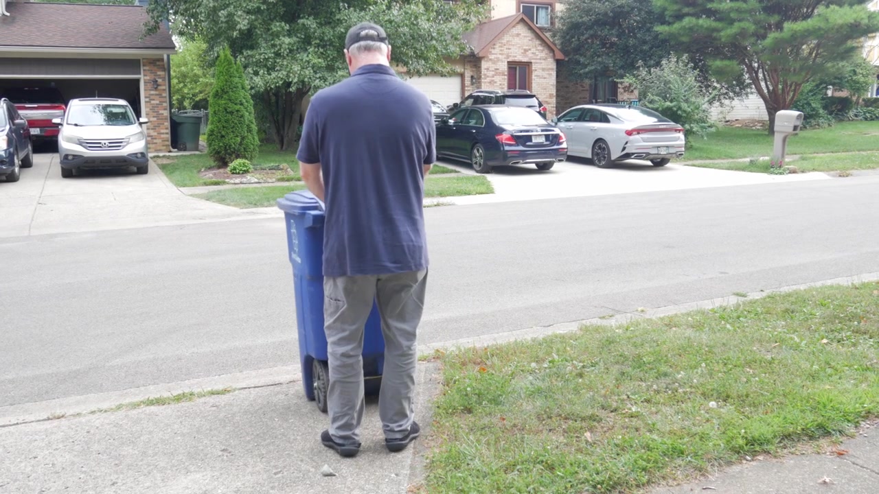 Man wheels blue recycling container to the curb for weekly pick-up