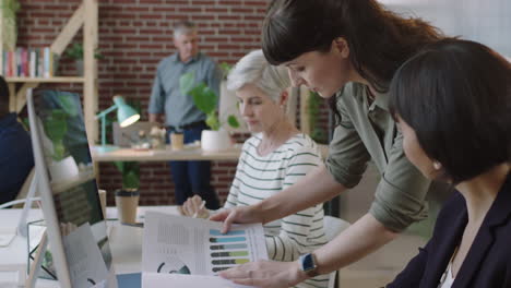 mature-mixed-race-business-woman-using-computer-in-modern-office-young-female-intern-showing-graph-research-diverse-team-collaborating-in-workspace