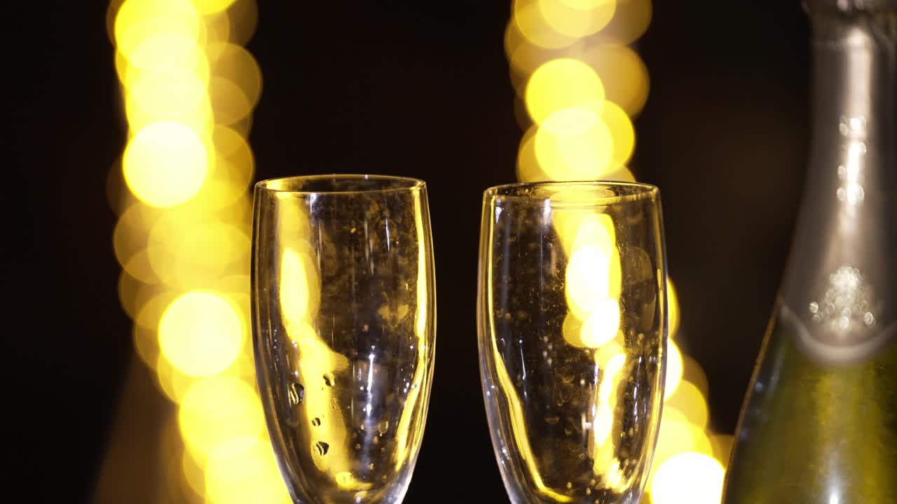 Close-up of two champagne glasses with golden bokeh lights in the background