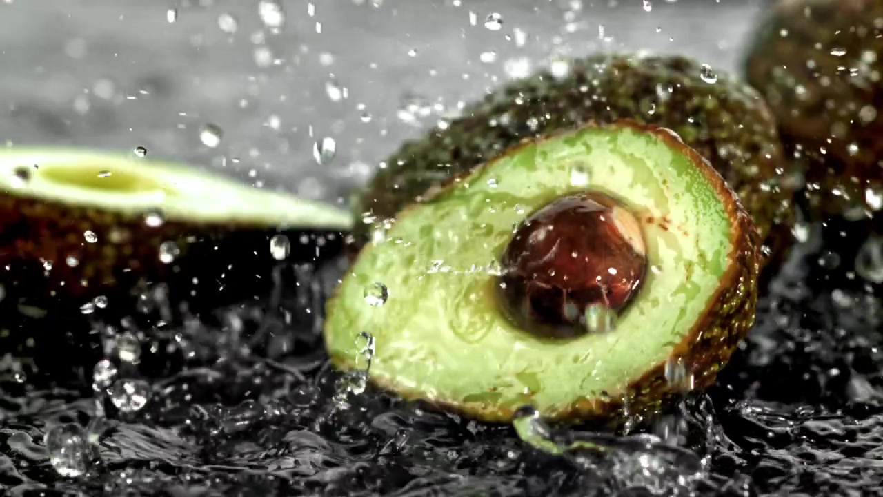 Vann plasker i sakte film på en halvert avokado