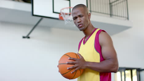 african american man holds a basketball, looking determined in a gym