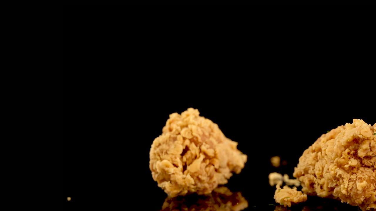 Golden, crispy fried chicken breasts and thighs rotate in slow motion against a black backdrop, with dramatic studio lighting and tight zoom for appetizing detail
