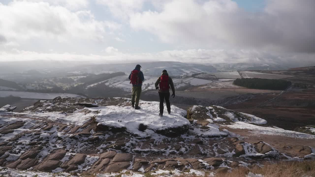 피크 디스트릭트의 얼어붙은 야생 시골 지역의 아름다운 풍경을 감상하며 눈 덮인 노두 위에 서 있는 두 남자