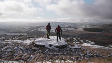 Dos-Hombres-Parados-En-Un-Afloramiento-Nevado-Admirando-Una-Hermosa-Vista-Del-Paisaje-De-Una-Extensión-Rural-Congelada-Y-Salvaje-En-El-Distrito-De-Los-Picos