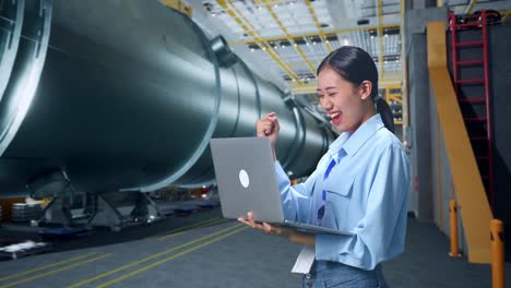 side view of happy asian business woman celebrating using laptop computer in pipe manufacturing factory