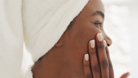 video of happy african american woman in robe moisturizing face