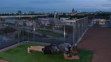 Guy-is-doing-Planks-on-a-Terrace-in-the-evening,-with-the-Danube-River-backdrop-in-Vienna,-Austria,-4K-time-lapse