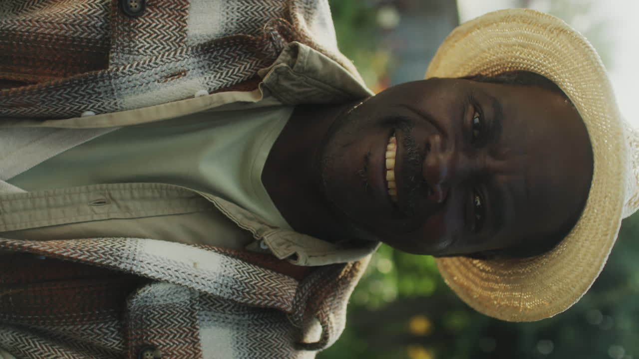 Close-up of a smiling man in a straw hat and plaid jacket