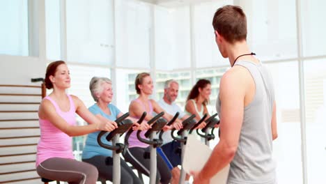 Instructor-De-Spinning-Sonriendo-A-La-Cámara-Frente-A-Su-Clase