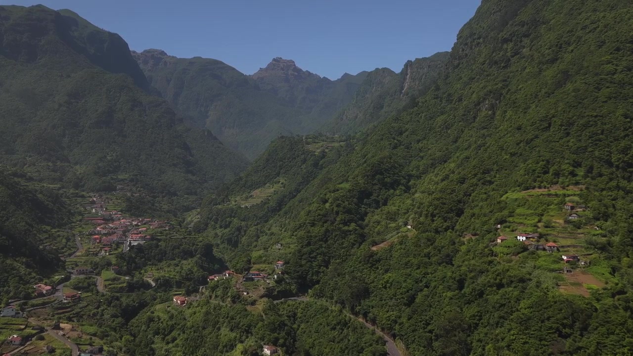 Ripresa con drone sopra il villaggio di Fajã do Penedo, incorniciato da imponenti montagne di foresta di alloro verde, luce solare che illumina campi terrazzati e una profonda valle nell'isola di Madeira, patrimonio UNESCO.