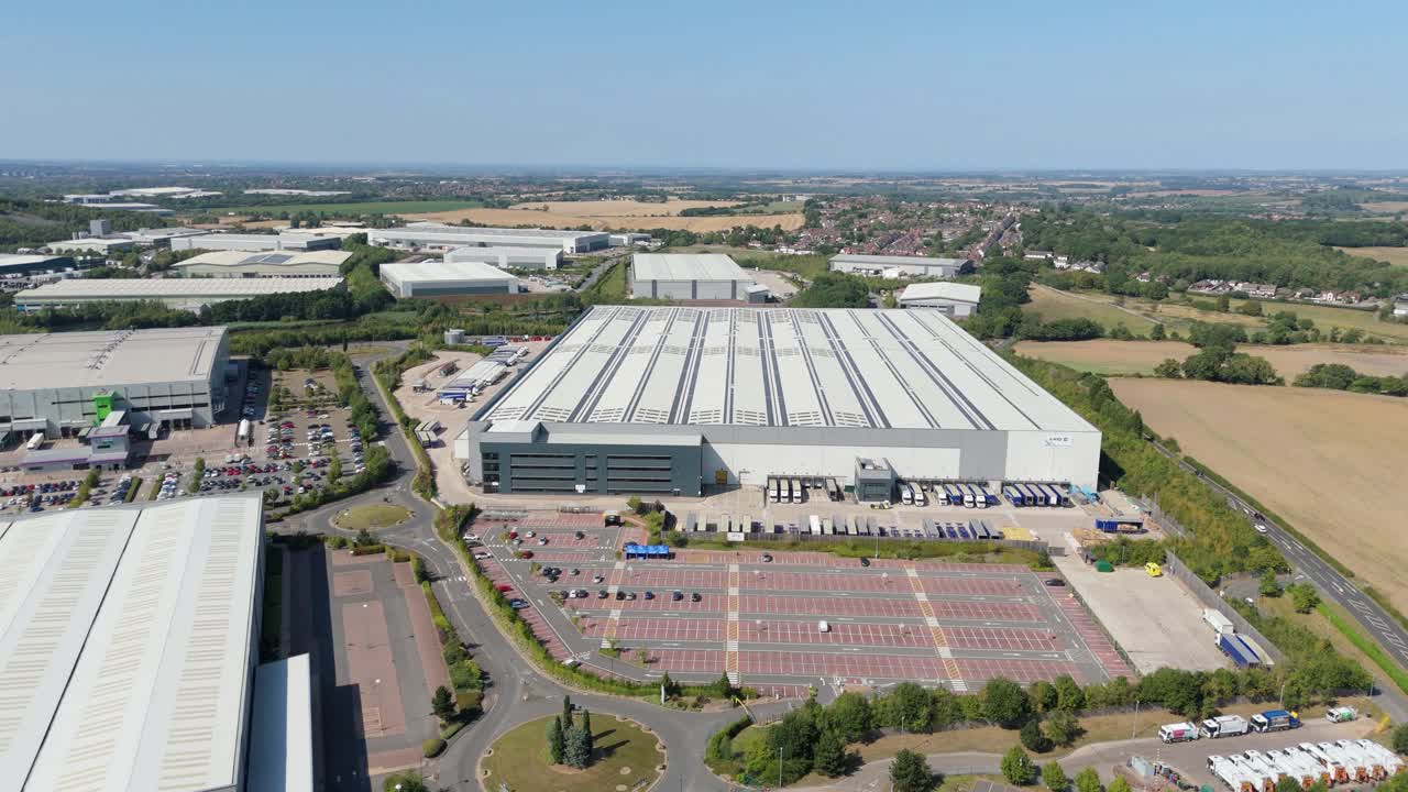 Drone aerial video of industrial warehouses, logistics hubs, factories, and retail park with parking lot surrounded by rural golden fields Tamworth UK