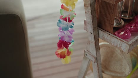 vibrant multicolor lei draped on a weathered wooden shelf beside party glasses and a straw hat
