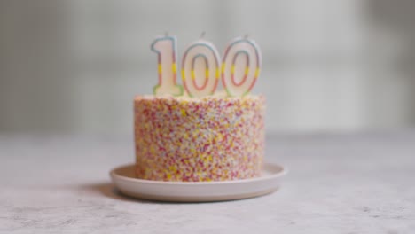 studio shot birthday cake covered with decorations and candle celebrating one hundredth birthday being lit