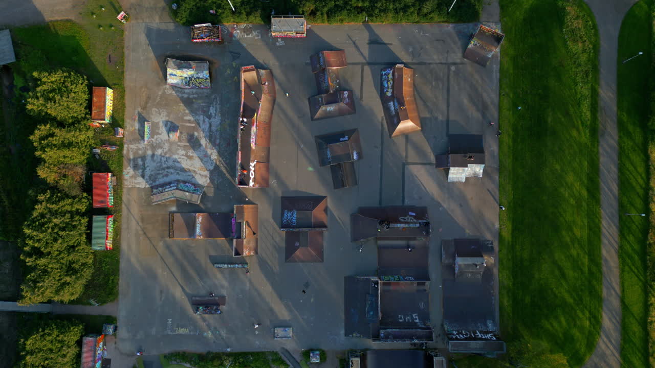 gran parque de patinaje de madera en un parque, con varias personas montando patinetas, scooters y bicicletas bmx, cámara fija