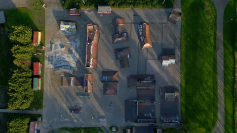 large wooden skate park in a park, with multiple people riding skateboards, scooters and bmx bikes, fixed camera