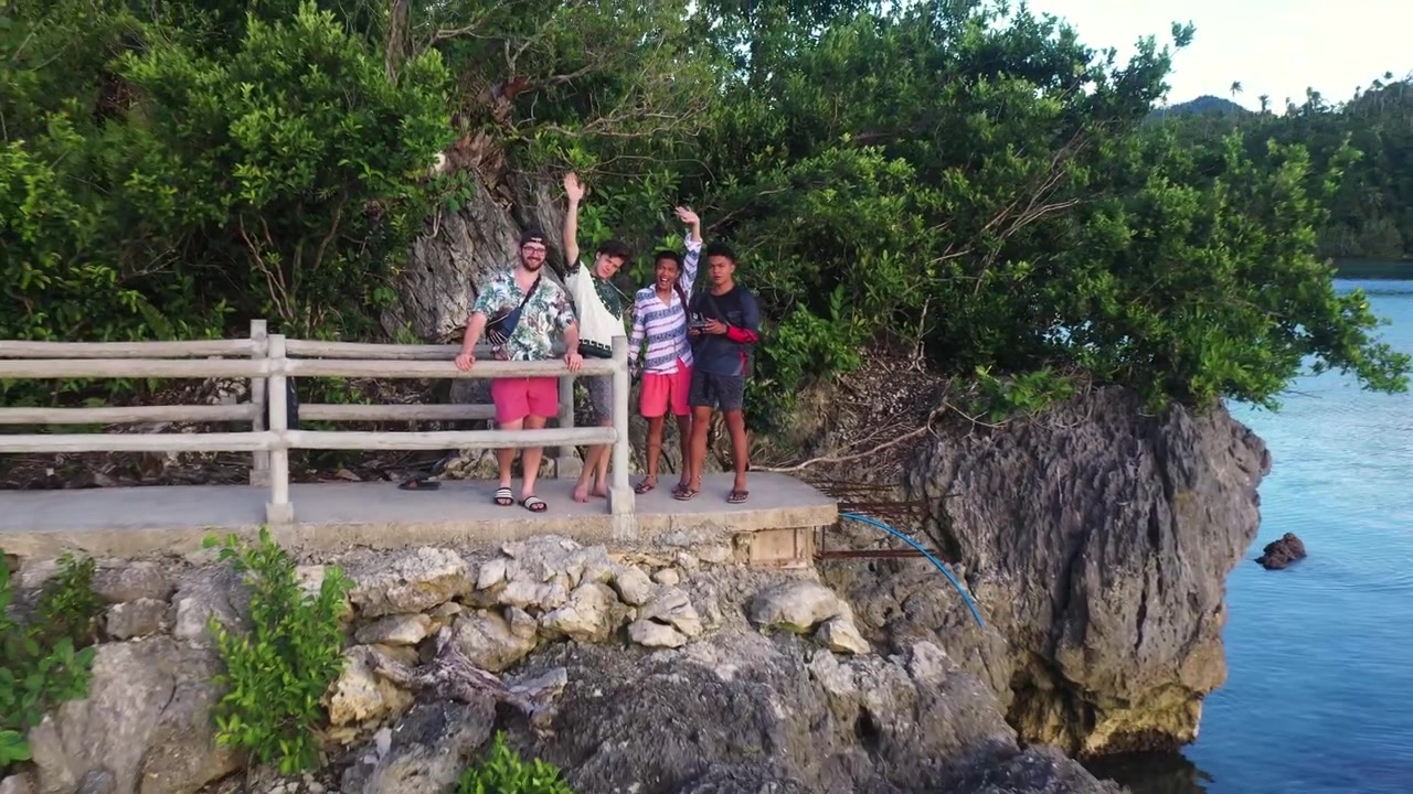 Quatro Amigos Turistas Felizes Em Pé Na Borda De Uma Enorme Rocha No Mar Com Grades Acenando Para O Drone Voador Durante Uma Viagem Para Liloan E Pintuyan Em Southern Leyte, Filipinas. - Tomada De Afastamento De Drone