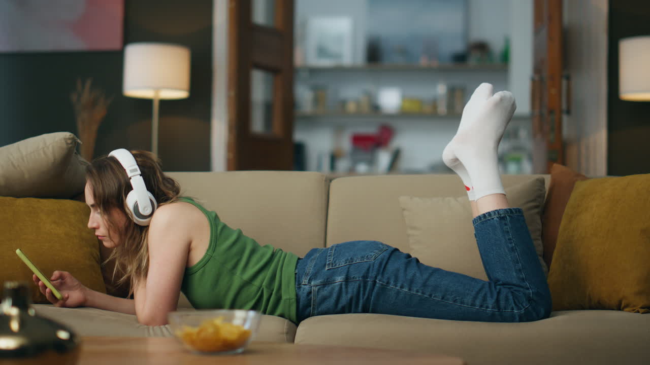 헤드폰을 듣는 학생, 캐스트를 듣고, 소파를 놓고, 음악을 즐기는 편안한 여인
