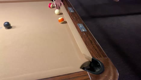 playing pool in a dark bar, hitting the orange object ball with a cue and hits the hole. playing billiards pool table under the white light.