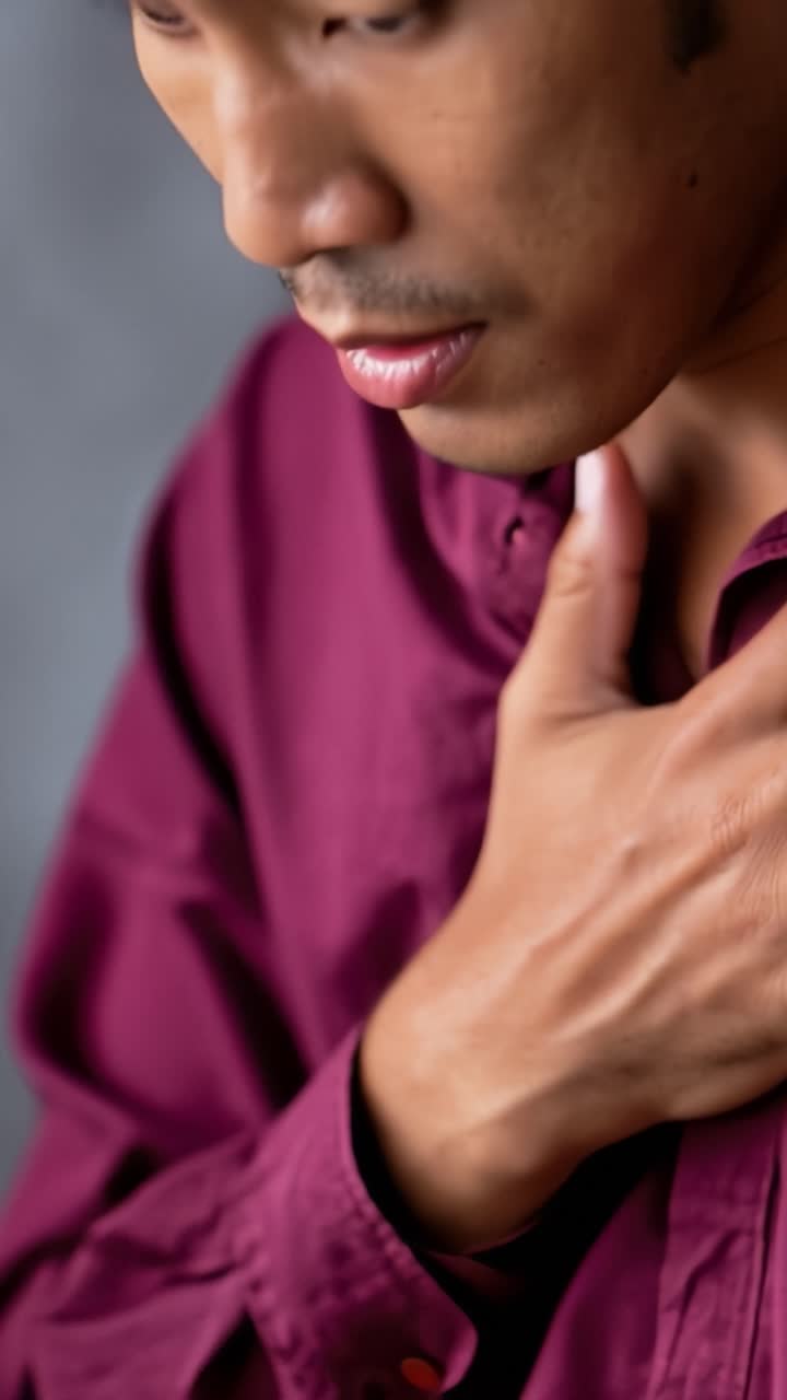 Una mano tocca il petto con disagio. La persona guarda in basso, stressata. Un primo piano mostra una sottile ansia. Ideale per immagini legate alla salute o alla medicina.