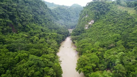 Drone-aerial-footage-of-Guatemalan-river-Rio-Cahabon-leading-up-to-Semuc-Champey-National-Park,-Guatemala-surrounded-by-bright-green-rainforest-hillsides-and-mountains