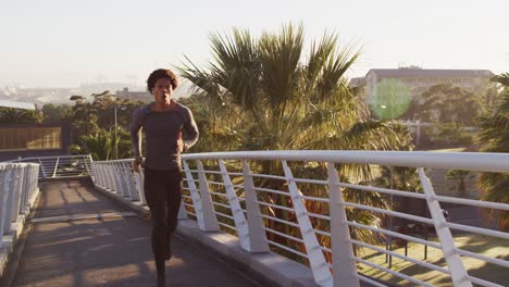 Fit-african-american-man-exercising-outdoors-in-city-wearing-earphones,-running-on-footbridge