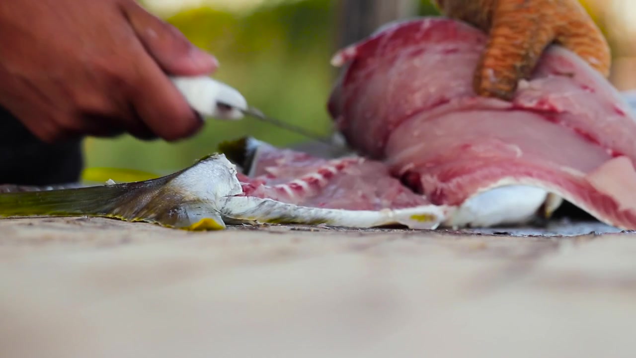 Fishmonger working on cutting board using fillet knife to gut yellowtail