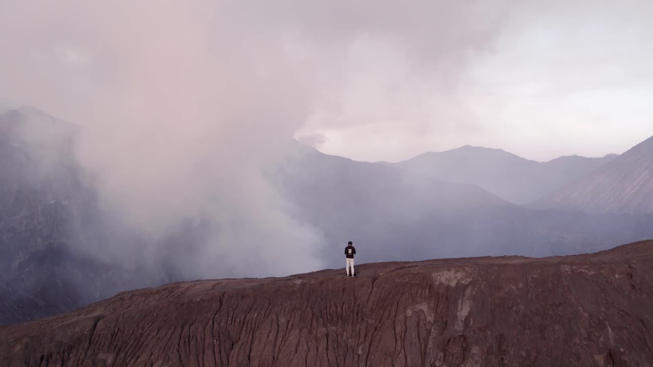 Cratere in eruzione del Bromo con un uomo che cammina all'alba