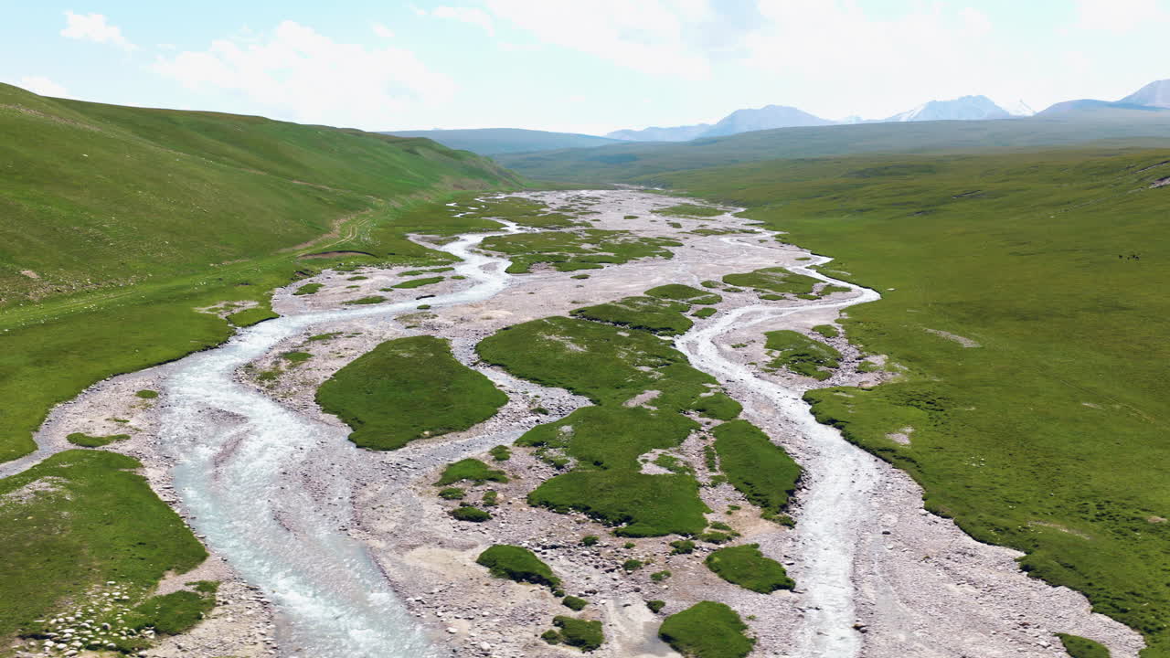 Den flettede Sary Jaz-flod med gletsjervand, der strømmer over stenet flodleje gennem en grøn bjergdal i Kirgisistan. Droneoptagelse fra siden