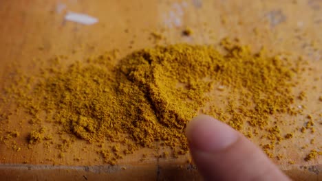 Finger-touching-curcuma-spice-on-wood