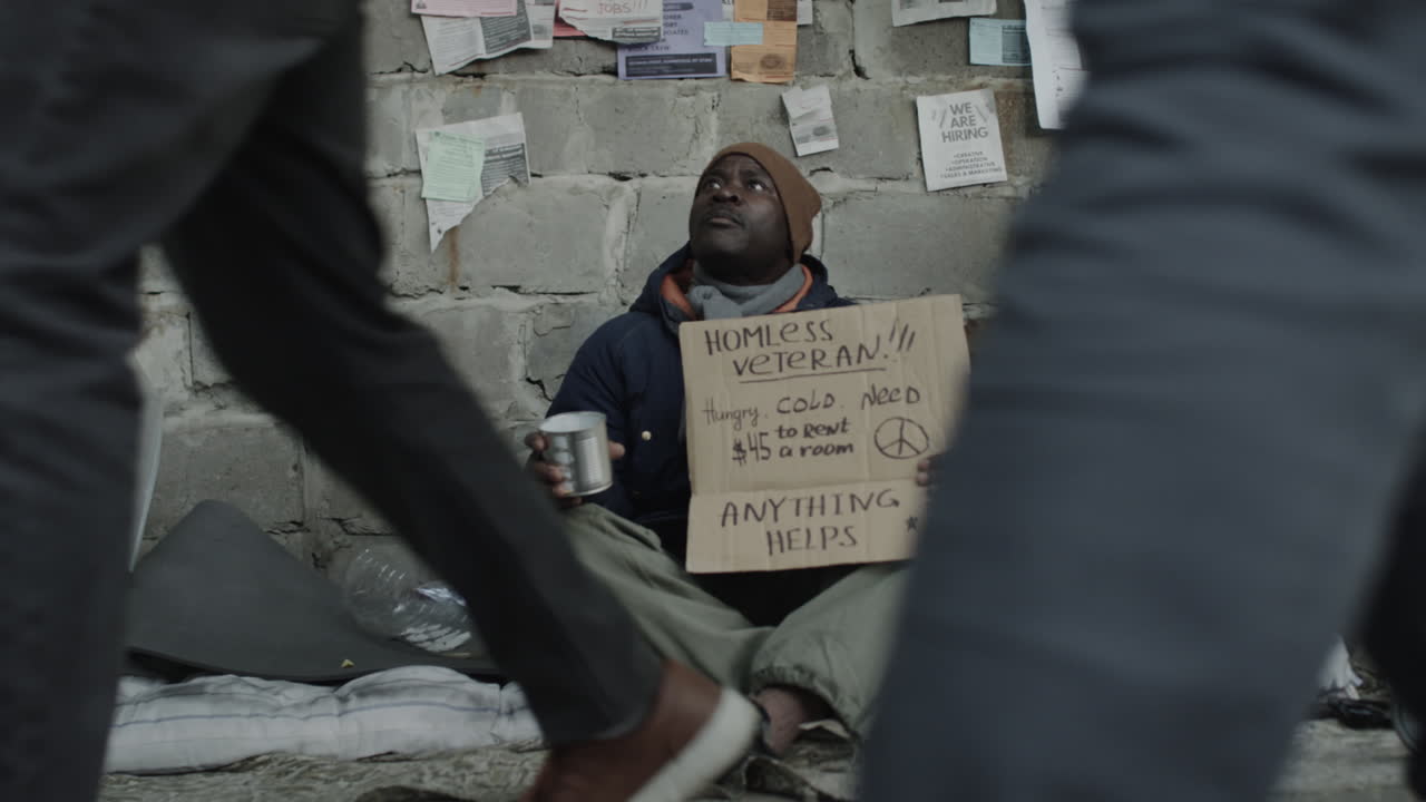 A homeless veteran sitting against a wall, holding a sign asking for help