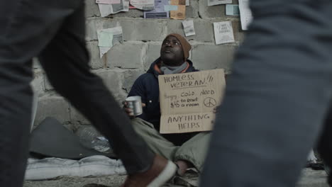 a homeless veteran sitting against a wall, holding a sign asking for help