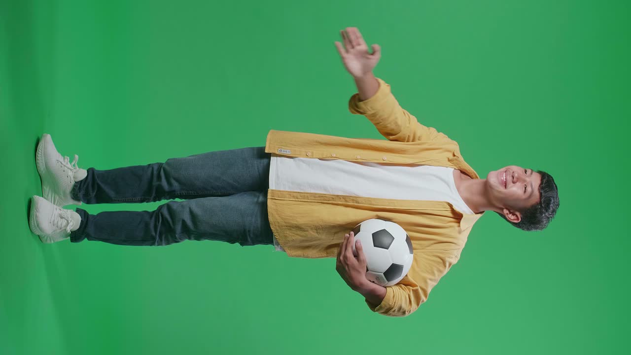 녹색 스크린 배경에서 축구를 응원하는 동안 을 고 웃는 공을 가진 아시아 소년의 전체 몸 측면 시각