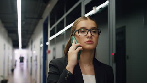 Confident-manager-speak-smartphone-corridor-closeup.-Beautiful-ceo-walk-office